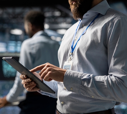 A man in a shirt and tie holds a tablet, looking engaged and focused on the device.