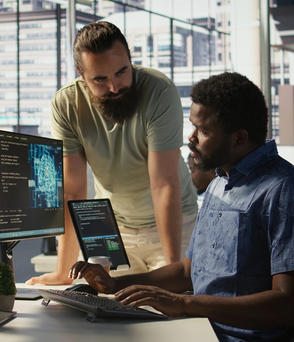 Two men collaborating on a computer in a modern office setting, focused on their work.