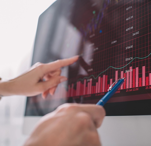 A person points at a computer screen displaying a graph, indicating data or trends.