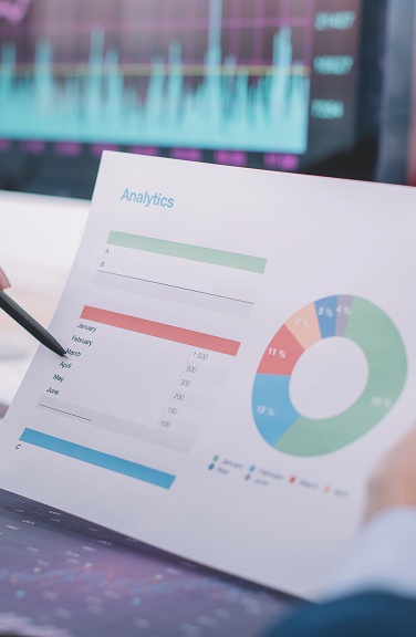 Businessman analyzing graphs and charts on a desk, holding a pen and paper, representing analytics and business strategy.