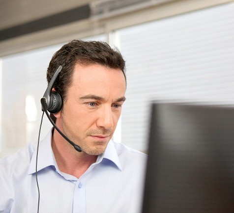 A man wearing a headset sits in front of a computer, focused on his work or a virtual meeting.
