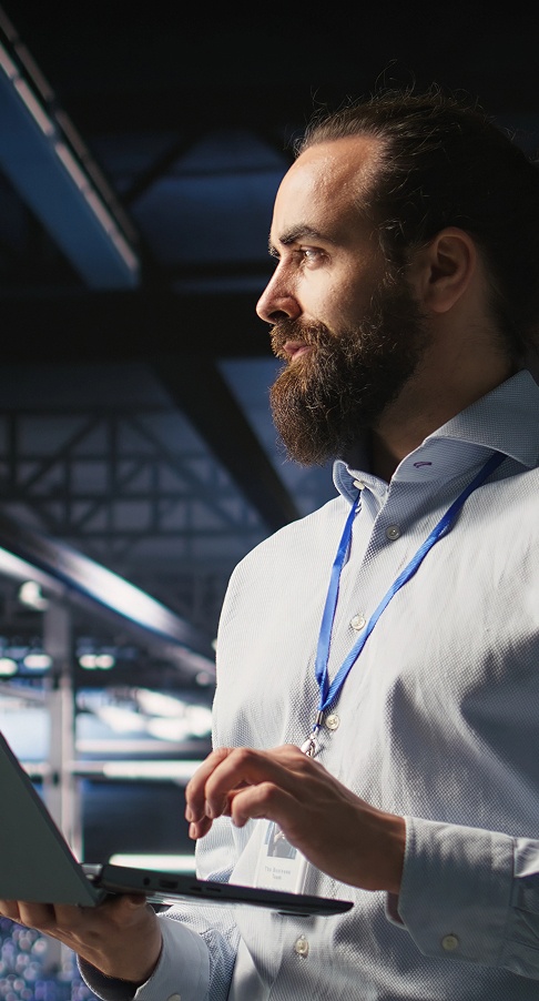 A man with a beard wearing a blue tie stands in front of a laptop, looking engaged and focused.