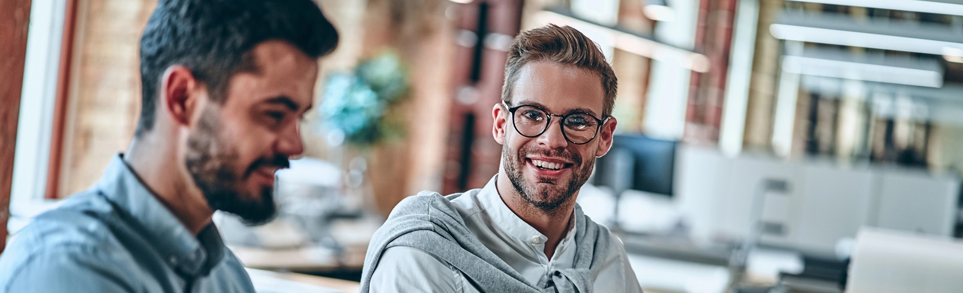 Two smiling men stand together in a bright office, conveying a friendly and professional atmosphere.