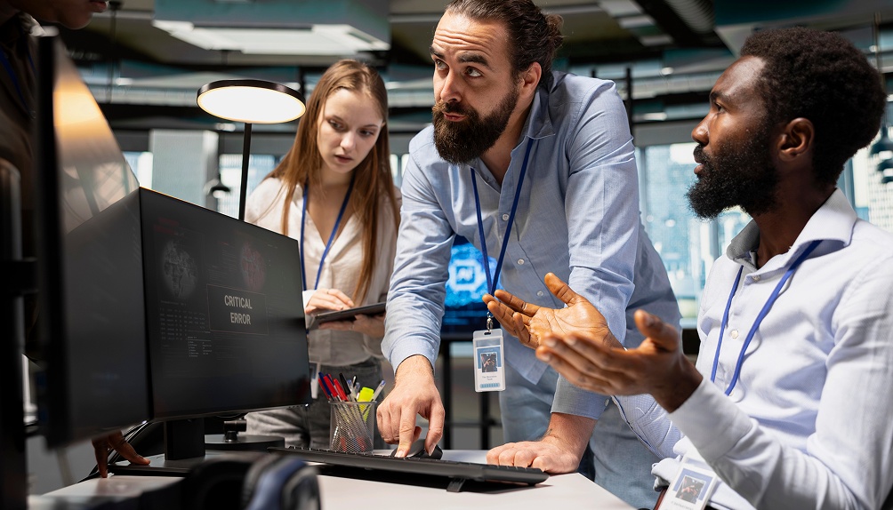 Three people are gathered around a computer screen, intently observing the display together.