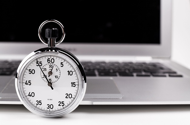A stopwatch rests on a desk beside an open laptop, indicating a focus on time management or productivity.