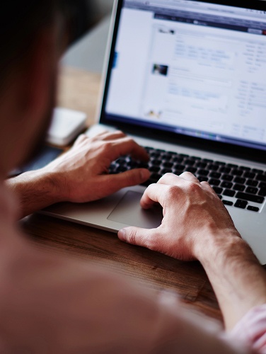 A person typing on a laptop computer, focused on the screen with hands on the keyboard.