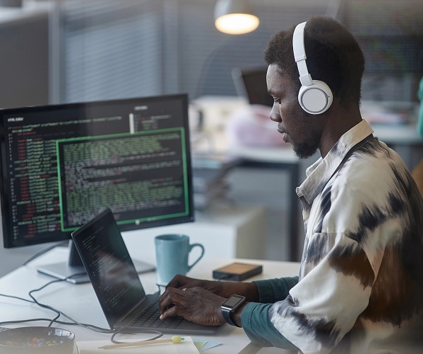 A man wearing headphones is focused on working at his computer.